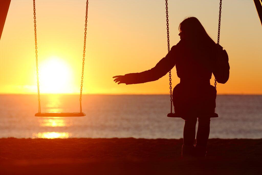 Eine Frau auf einer Schaukel am Strand schaut auf die leere Schaukel neben sich