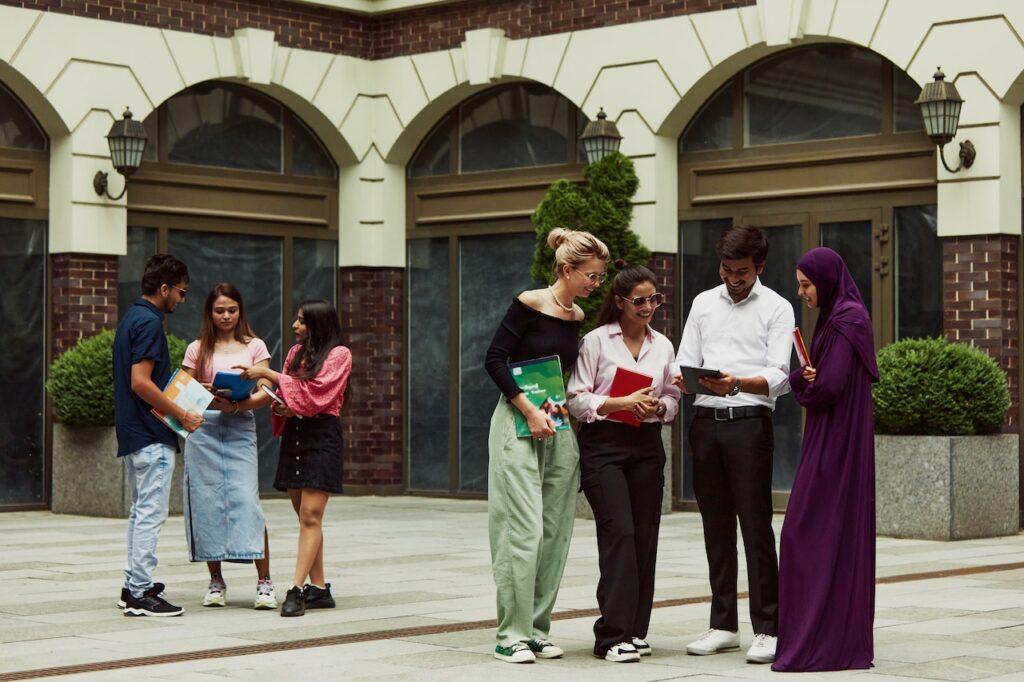 Eine diverse Gruppe von Schülern steht vor einem eleganten Schulgebäude, diskutiert gemeinsam und tauscht Lernmaterialien aus.