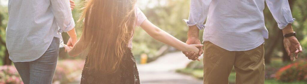 Eltern gehen mit Kind Hand in Hand durch den Park – Symbol fuer Zusammenarbeit nach Trennung, Kontext Rechtsanwalt Familienrecht Bonn